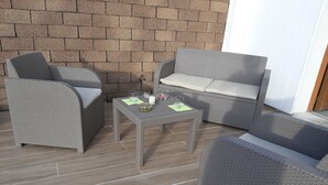 A patio area with wicker furniture, including a sofa and chairs, and a small table with a glass and a bowl.