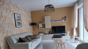Un salon moderne avec un canapé, une télévision et un petit coin repas. Les équipements comprennent un garage, un parking privé et un jardin.