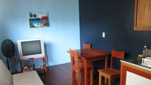 Een woonkamer met een bank, een houten eettafel met stoelen, een televisie op een meubel en een keuken met een spoelbak.