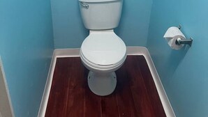 Un baño pequeño con inodoro blanco, suelo de madera y paredes azul claro.