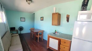 Un espacio habitable compacto con sofá, una mesa de comedor con sillas, una kitchenette con refrigerador y un ventilador de techo.