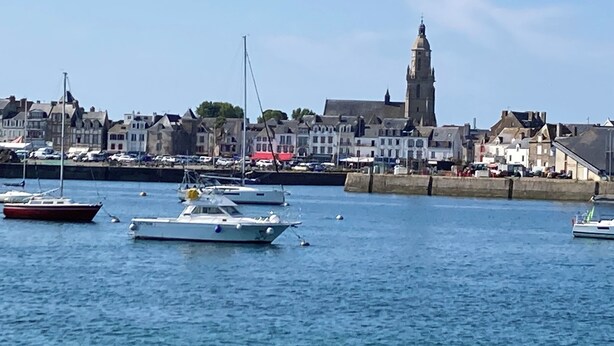 Un puerto con barcos, una destacada torre de iglesia y edificios residenciales a lo largo del paseo marítimo.