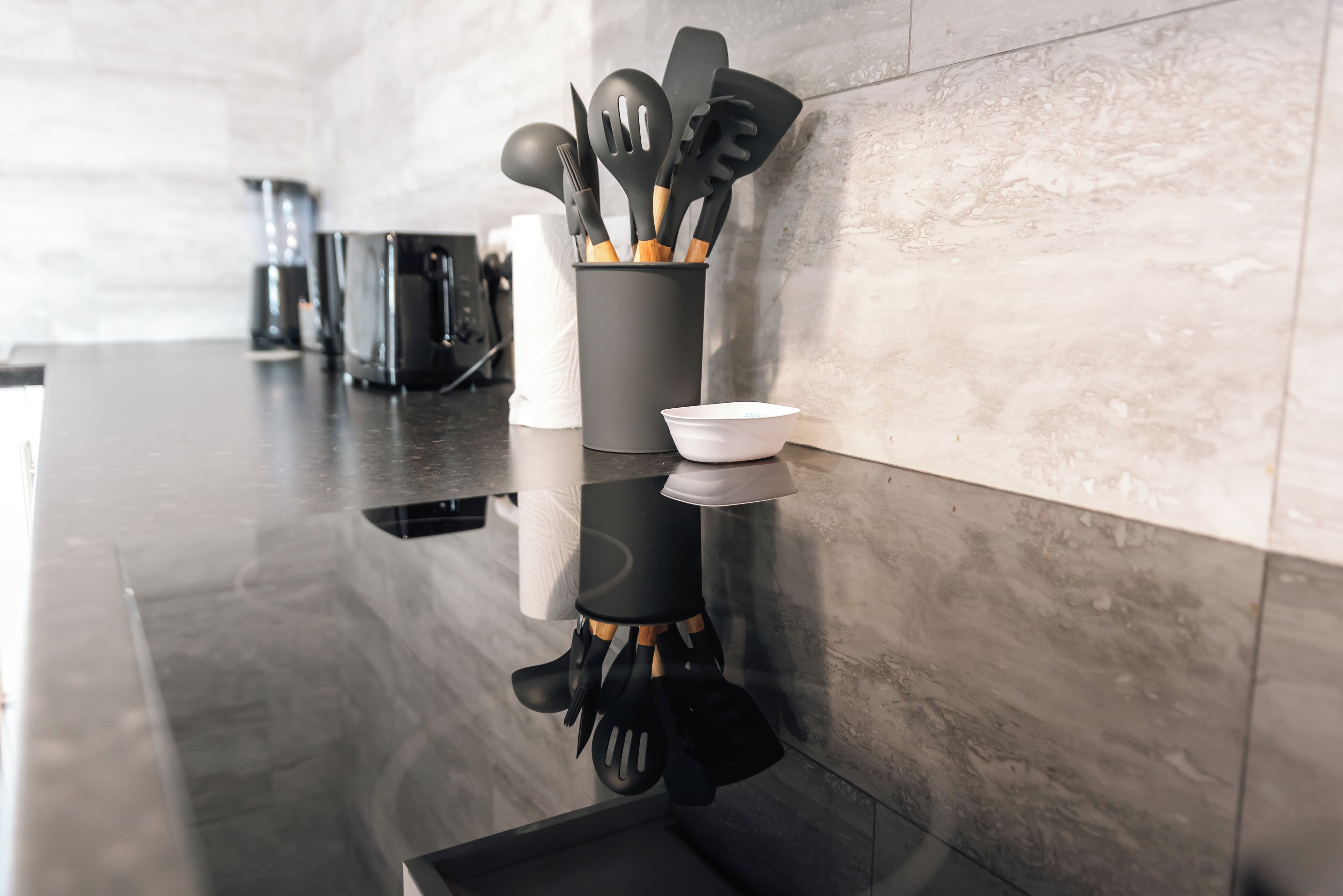A kitchen with a black countertop, a black utensil holder, and a white bowl.