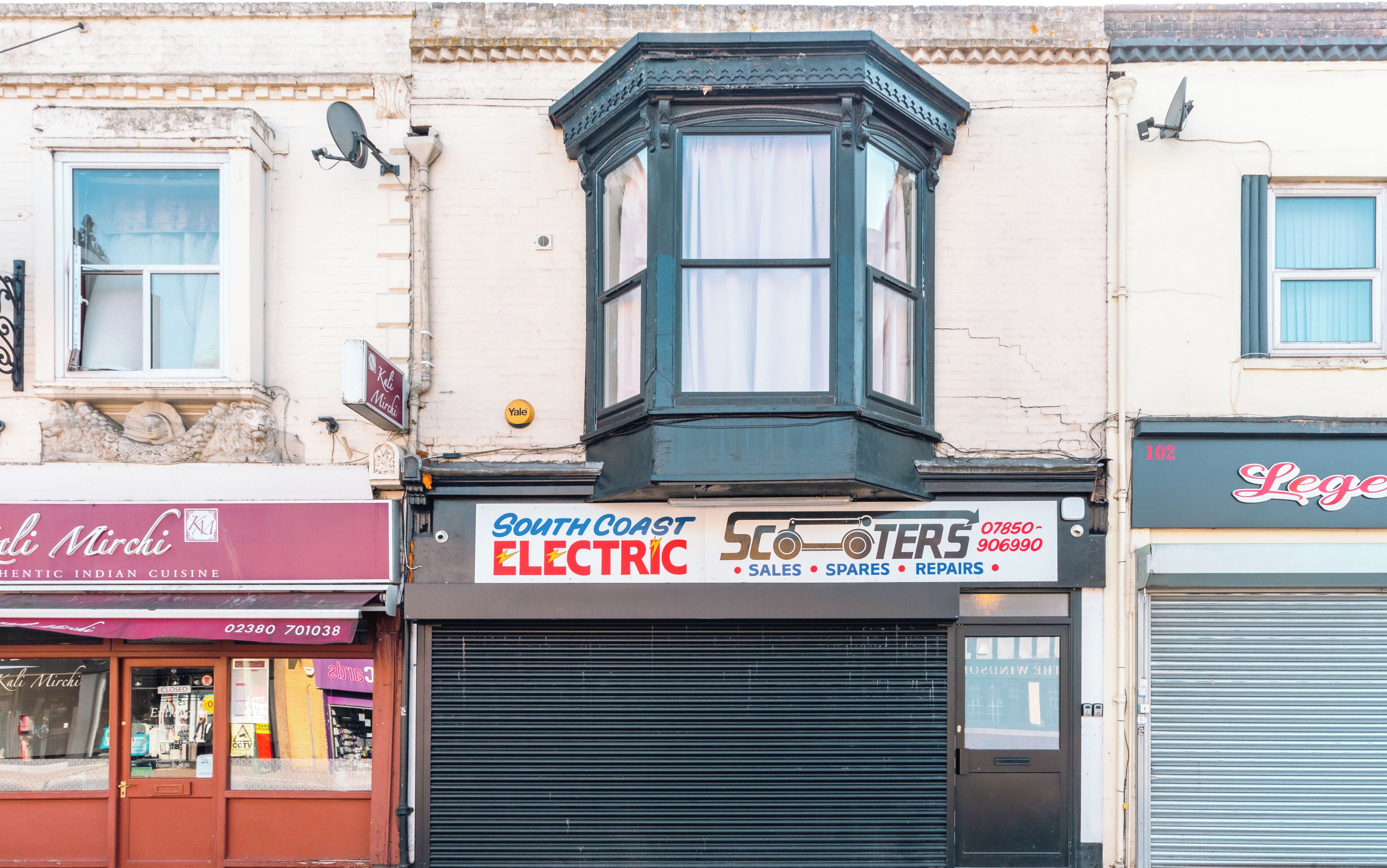A corner building with a bay window, a closed shuttered shop, and a sign for 'South Coast Electric'.