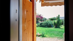 A wooden door leading to a garden with a table and chairs, a pink flowering tree, and a grassy area. - Agritourism. Accommodation x 2 people with outdoor kitchen, garden view (Mazzarino)