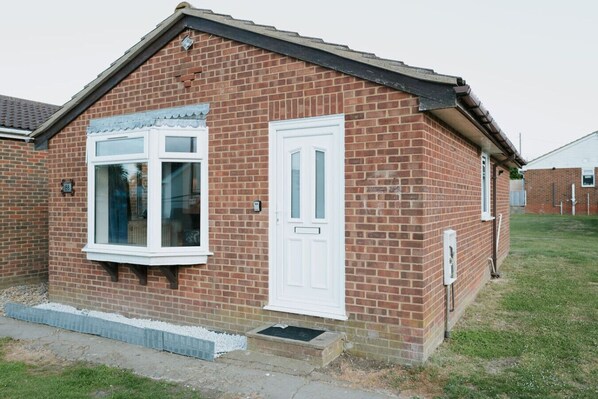 A small brick house with a white front door and a bay window.