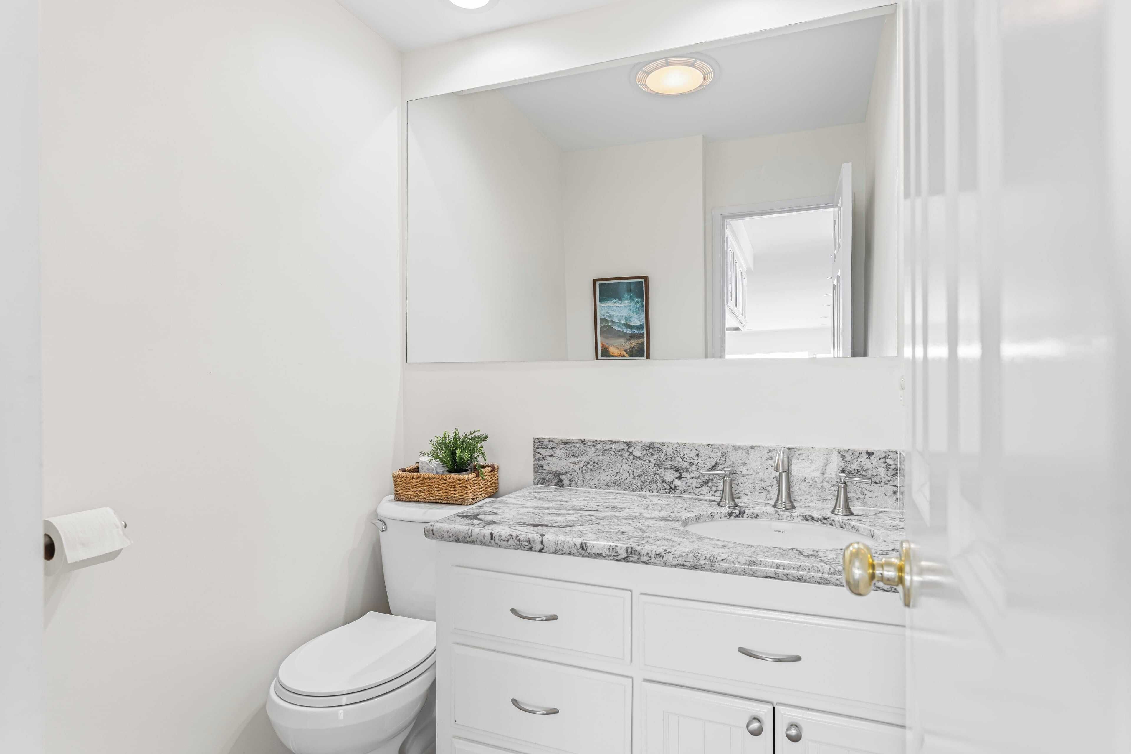 A modern bathroom with a white toilet, a marble countertop sink, and a large mirror above the sink.