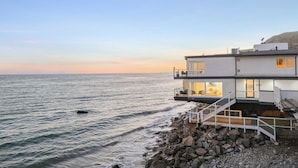 Una casa costera moderna con un balcón que da al mar, construida sobre terreno rocoso.