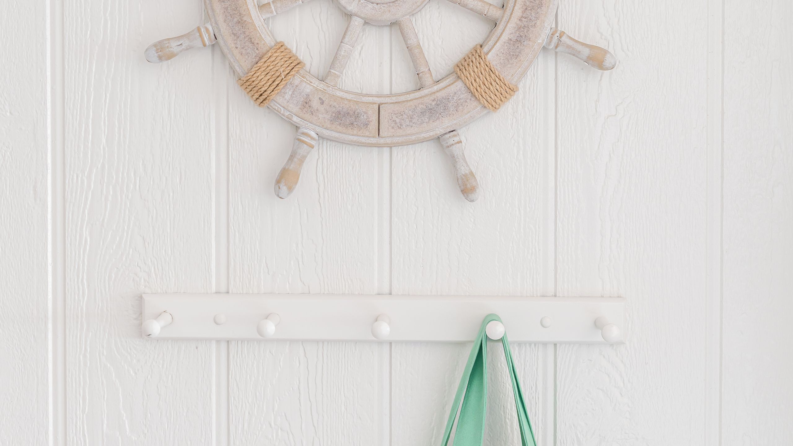 A white wall with a wooden ship's wheel and a white coat rack with hooks.