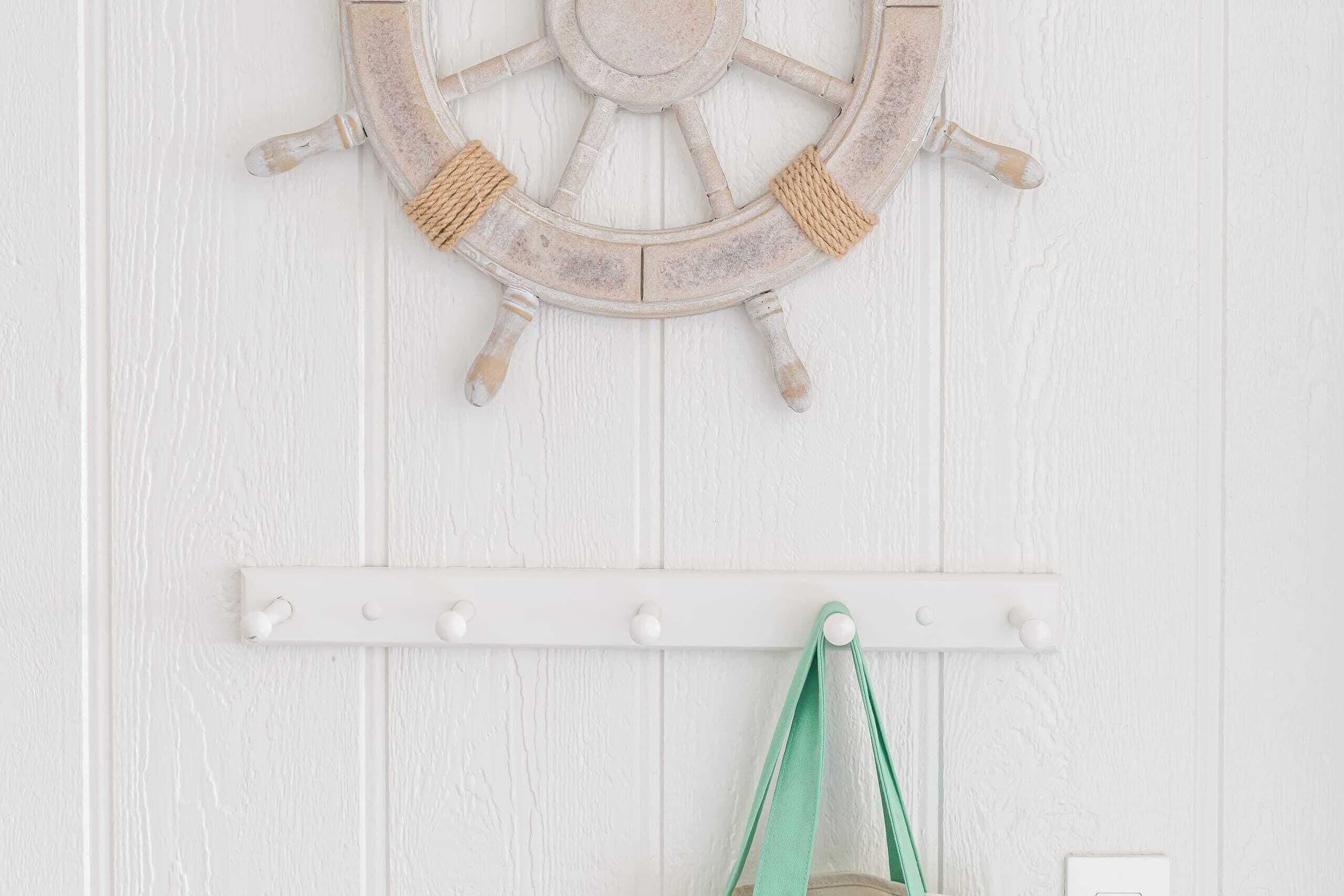 Een witte houten wand met een stuurwiel decoratie en een witte kapstok met haken.