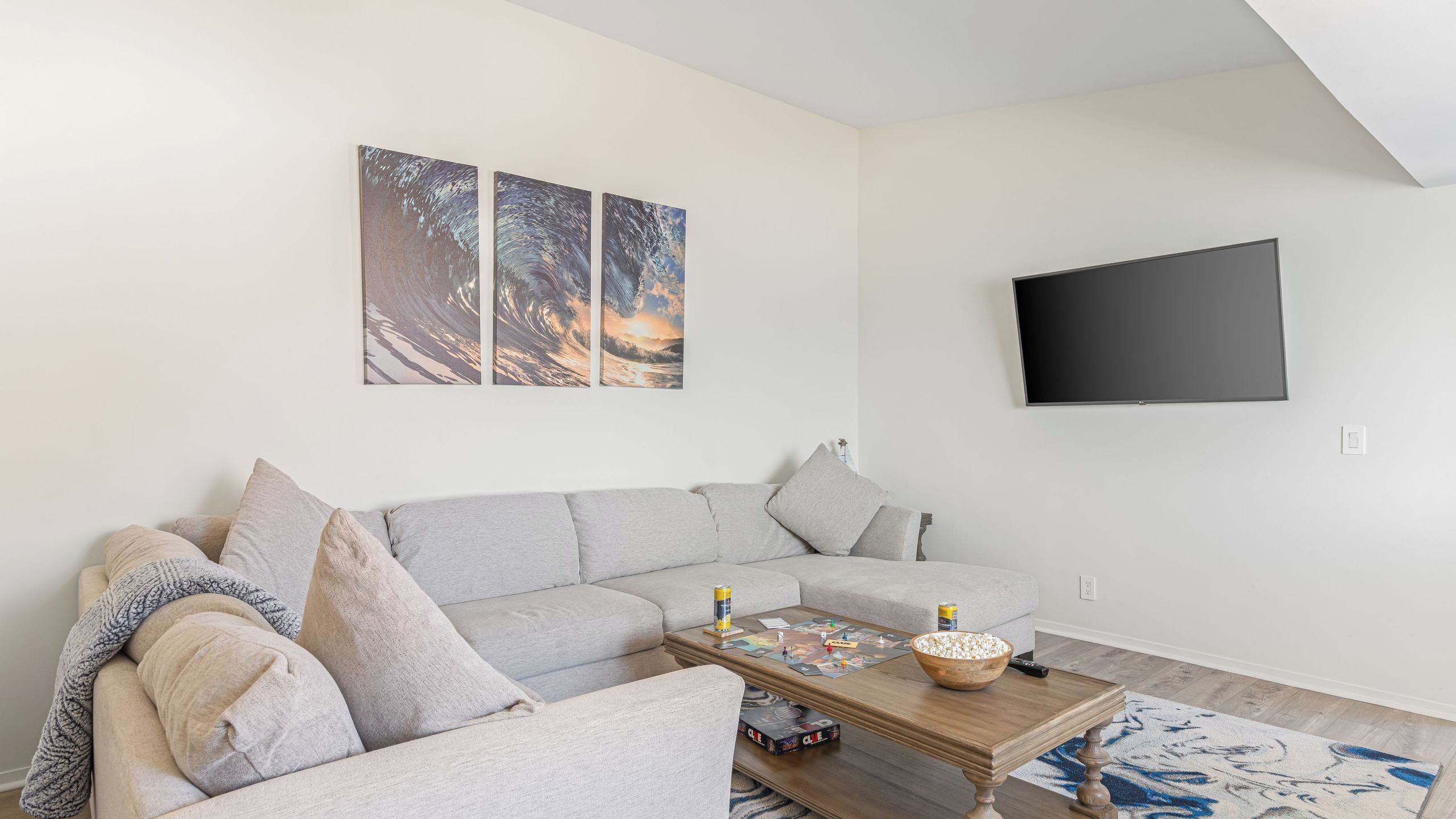 Un salon comprenant un canapé d’angle, une table basse avec des jeux de société, un téléviseur à écran plat et des œuvres d’art accrochées au mur.