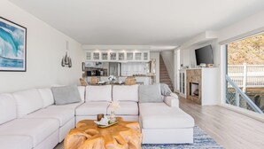 Una sala de estar moderna con un sofá seccional, una mesa de centro de madera y una cocina al fondo.