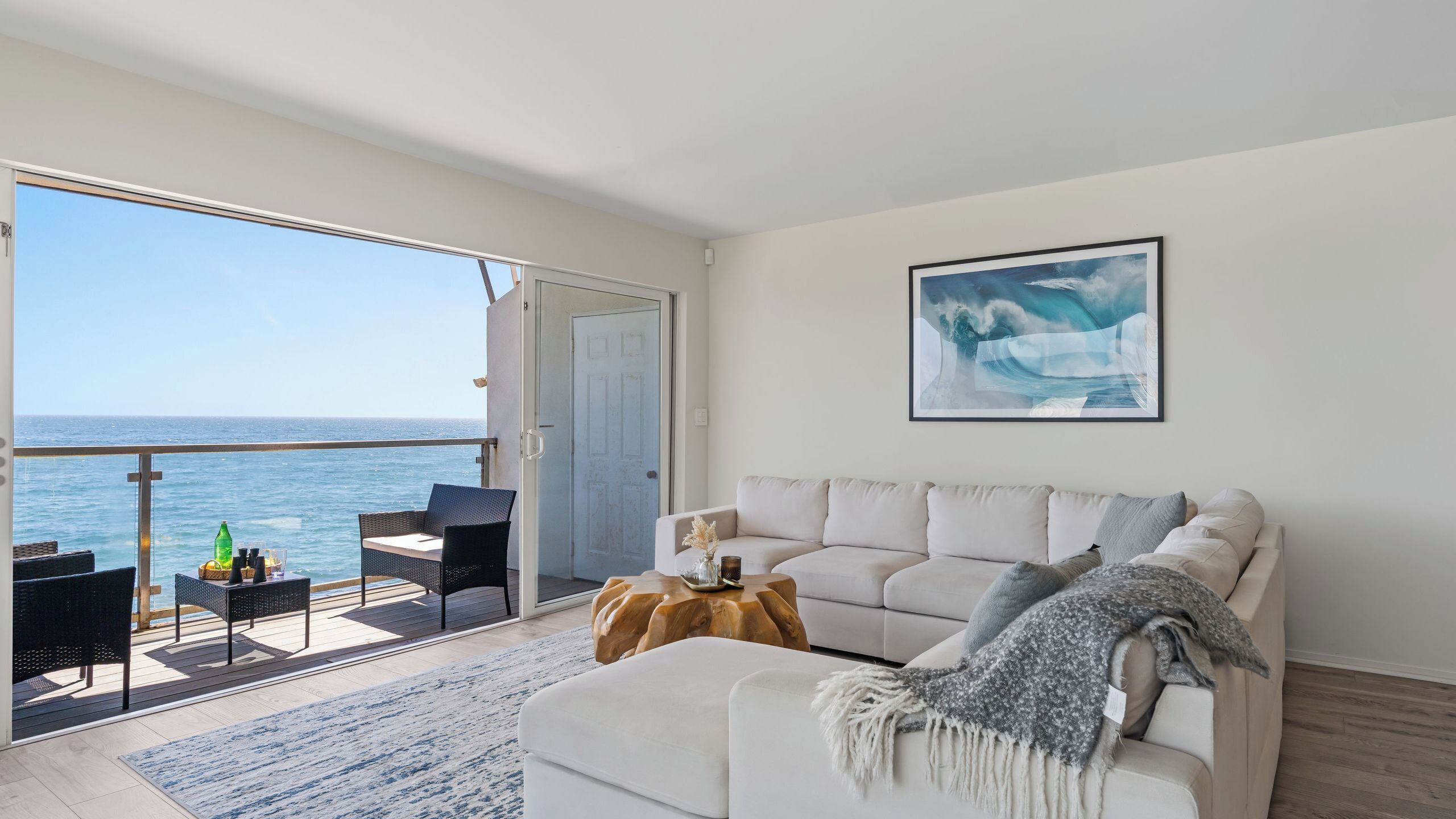 A balcony with a view of the sea, a white sofa, and a wooden coffee table.