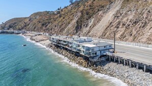 Una propiedad costera con varios edificios conectados a lo largo de la orilla, que incluye un muelle y un camino que lleva a la playa.