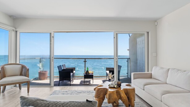 Un salón moderno con un amplio ventanal corredera que da a un balcón con vistas al océano.