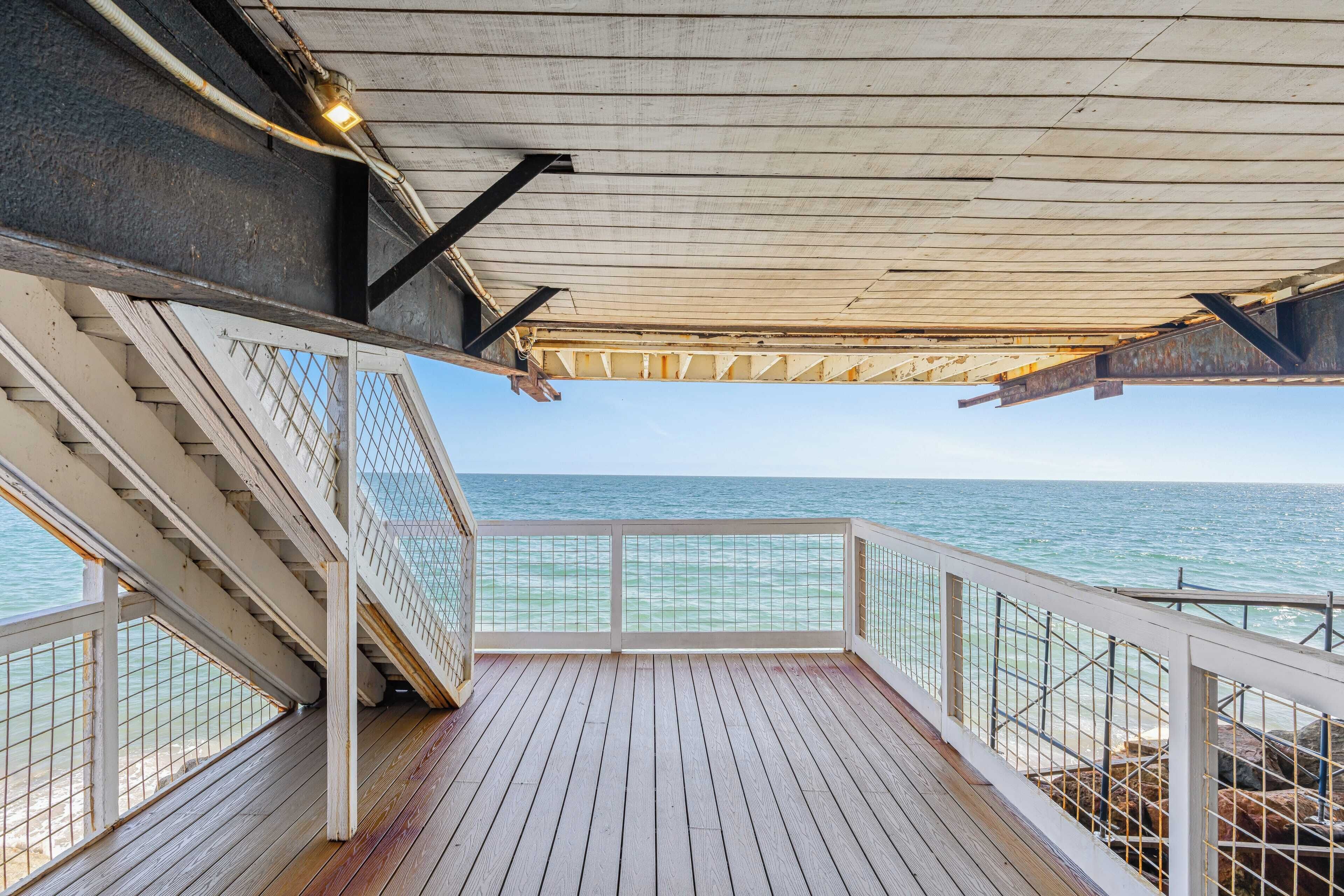 Una terraza de madera con barandilla que da al mar.