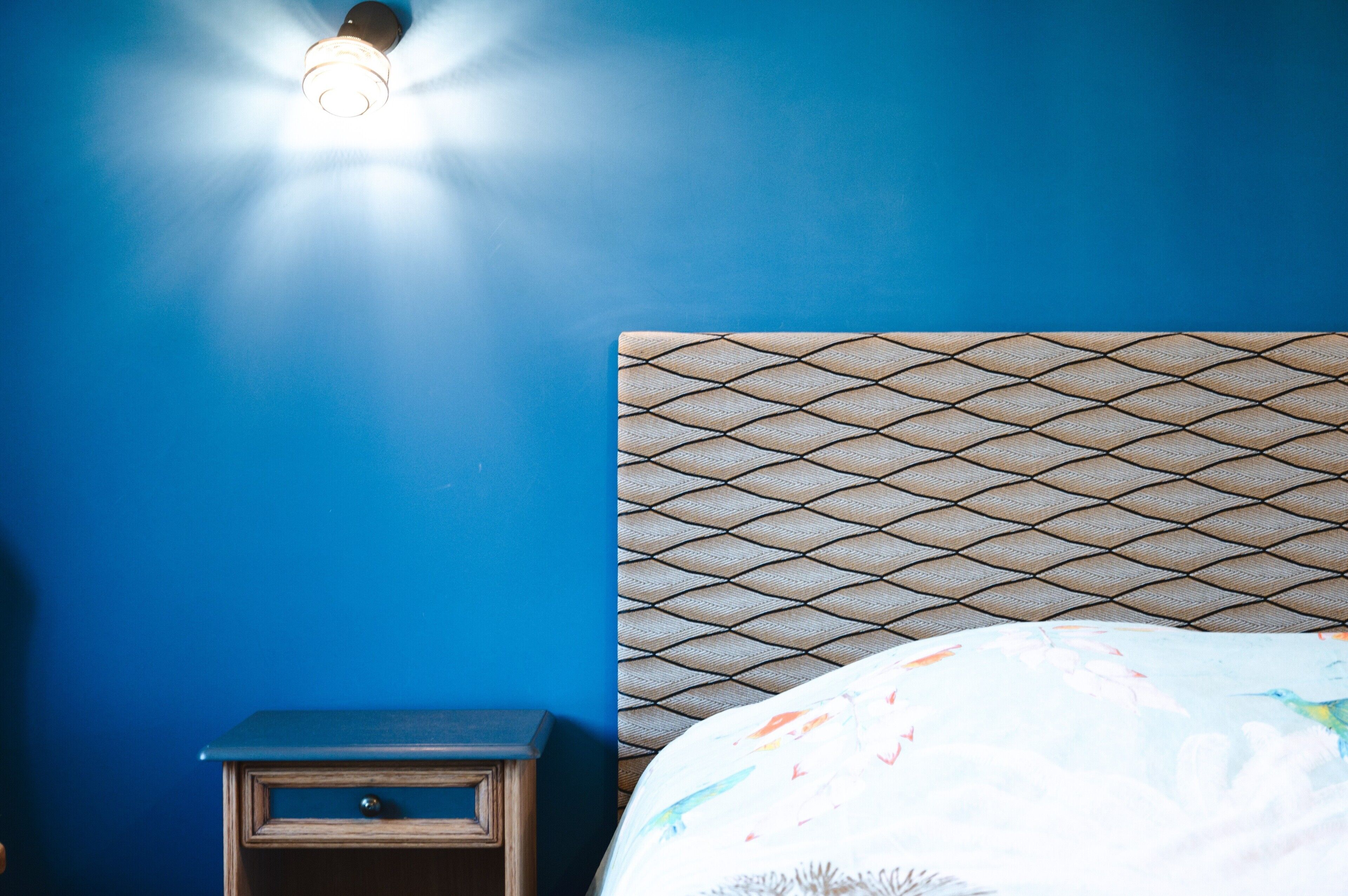 A room with a blue wall, a patterned headboard, a bedside table, and a bed with a colorful bedspread.