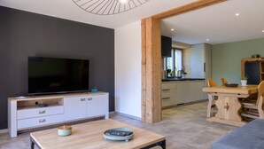 Ein modernes Wohnzimmer mit Flachbildfernseher, Holzes Esstisch und einer Küche im Hintergrund.