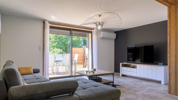 Ein modernes Wohnzimmer mit Sofa, Fernseher und bodentiefen Glasschiebeflügeln zum Außenbereich.