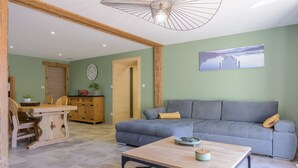 Ein Wohnzimmer mit einer Couch, einem Holztisch, einem Esstisch und einer Küchenzeile mit Schränken und einer Uhr.