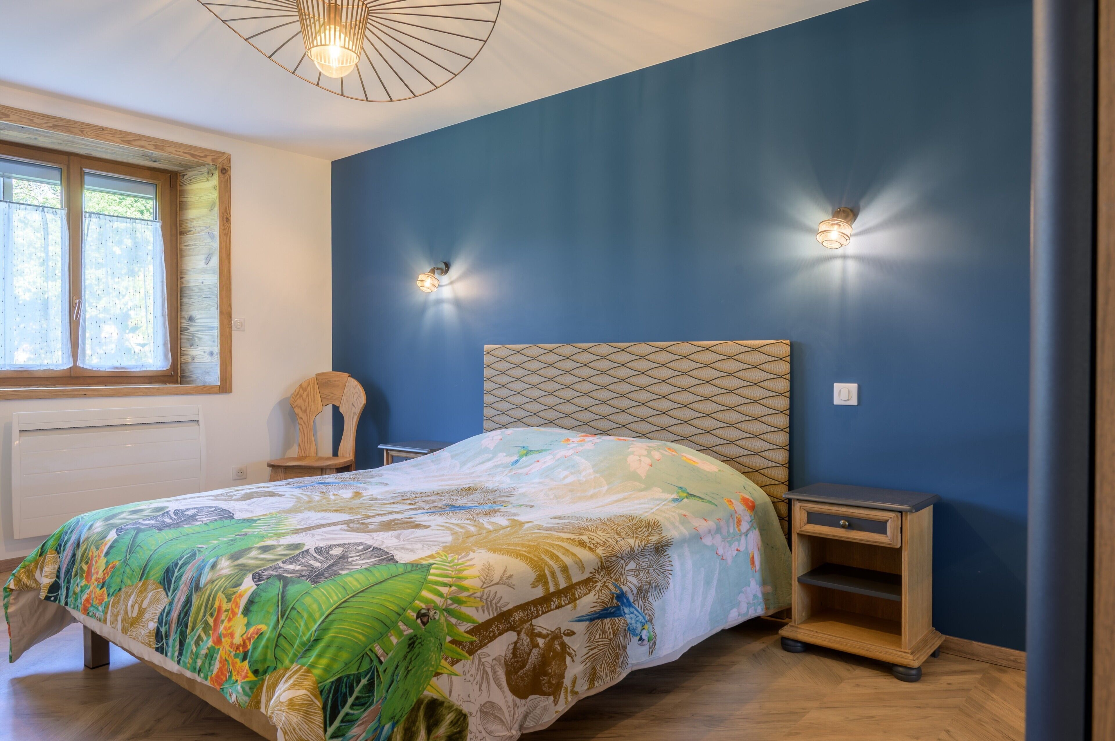 Una camera da letto con un letto, due comodini, una finestra con tende e un lampadario.