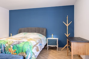 A bedroom with a bed, nightstand, desk, and coat rack. - Chez neous – Welcoming Apartment in a Peaceful Farm Setting (Dommartin-lès-Remiremont)
