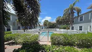 A pool area surrounded by white fences, lush greenery, and a clear blue sky.