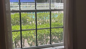 A window with a view of a white picket fence, green foliage, and a blue umbrella.