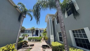 A courtyard with palm trees, a paved walkway, and a building with a gray facade and white trim.
