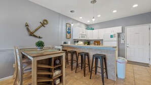A kitchen with white cabinets, a wooden dining table with four stools, a potted plant, and a hanging light fixture. - In the Middle of it All -2 Pools,Grill,Fishing,Boat Launch,Boat rental next door (Osage Beach)