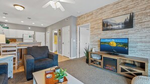 A modern living room with a flat-screen TV, comfortable seating, a fireplace, and a kitchen area in the background. - In the Middle of it All -2 Pools,Grill,Fishing,Boat Launch,Boat rental next door (Osage Beach)