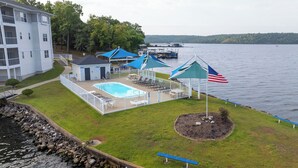 A pool area with a view of the lake, a flag, and a building in the background. - In the Middle of it All -2 Pools,Grill,Fishing,Boat Launch,Boat rental next door (Osage Beach)