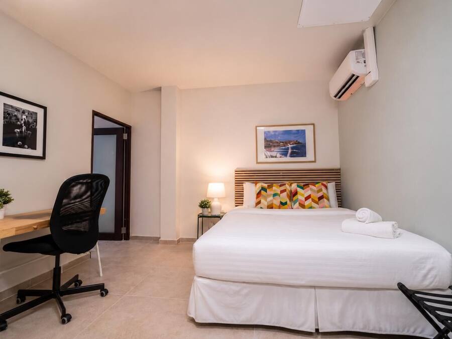 A hotel room with a bed, a desk, a chair, a lamp, and a picture on the wall.