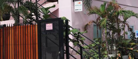 Un edificio rosa con toldo verde, entrada protegida por una reja y un cartel que indica la recepción.