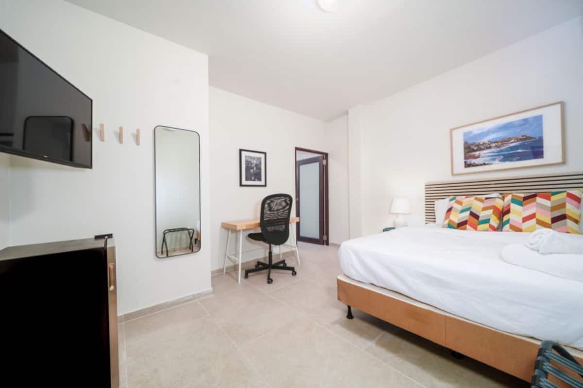 A hotel room with a bed, a desk, a chair, a TV, and a framed picture on the wall.