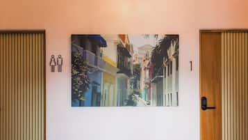 A hallway with a large painting of colorful buildings, a door with a keypad lock, and a toilet sign.
