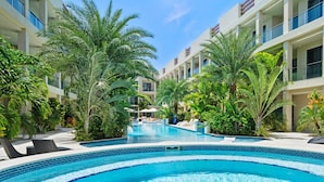 A swimming pool surrounded by lush greenery and modern buildings. - 1BR 1BA Condo w Pool/Jacuzzi/Gym (Noord)