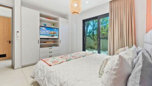 A bedroom with a bed, a wardrobe, a TV, and a sliding glass door to a garden. - 1BR 1BA Condo w Pool/Jacuzzi/Gym (Noord)