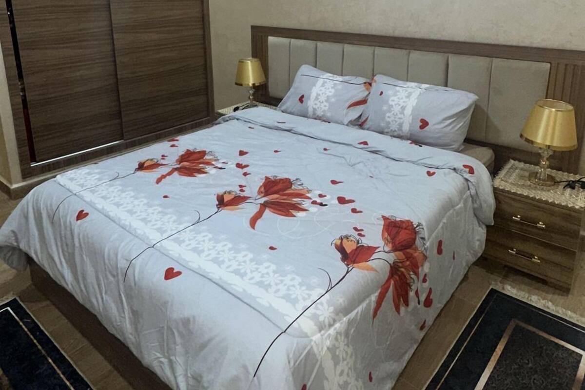 A neatly made bed with a floral bedspread, a wooden headboard, and two bedside lamps.