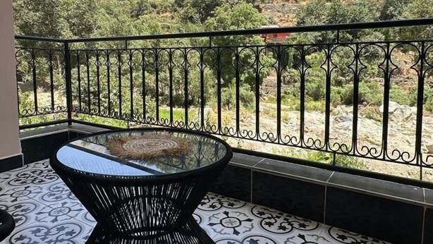 A balcony with a glass-top table and a patterned floor, overlooking a mountainous landscape. - Kasbah Itran Appart (Sti Fadma)