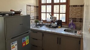 A compact kitchen with a refrigerator, stove, sink, and window. - Kasbah Itran Appart (Sti Fadma)