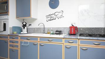 Een keuken met blauwe kastjes, een wit aanrecht, een klok, een koffiezetapparaat en een fornuis.