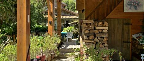 A wooden covered outdoor area with potted plants, a stone staircase, and a stack of firewood.