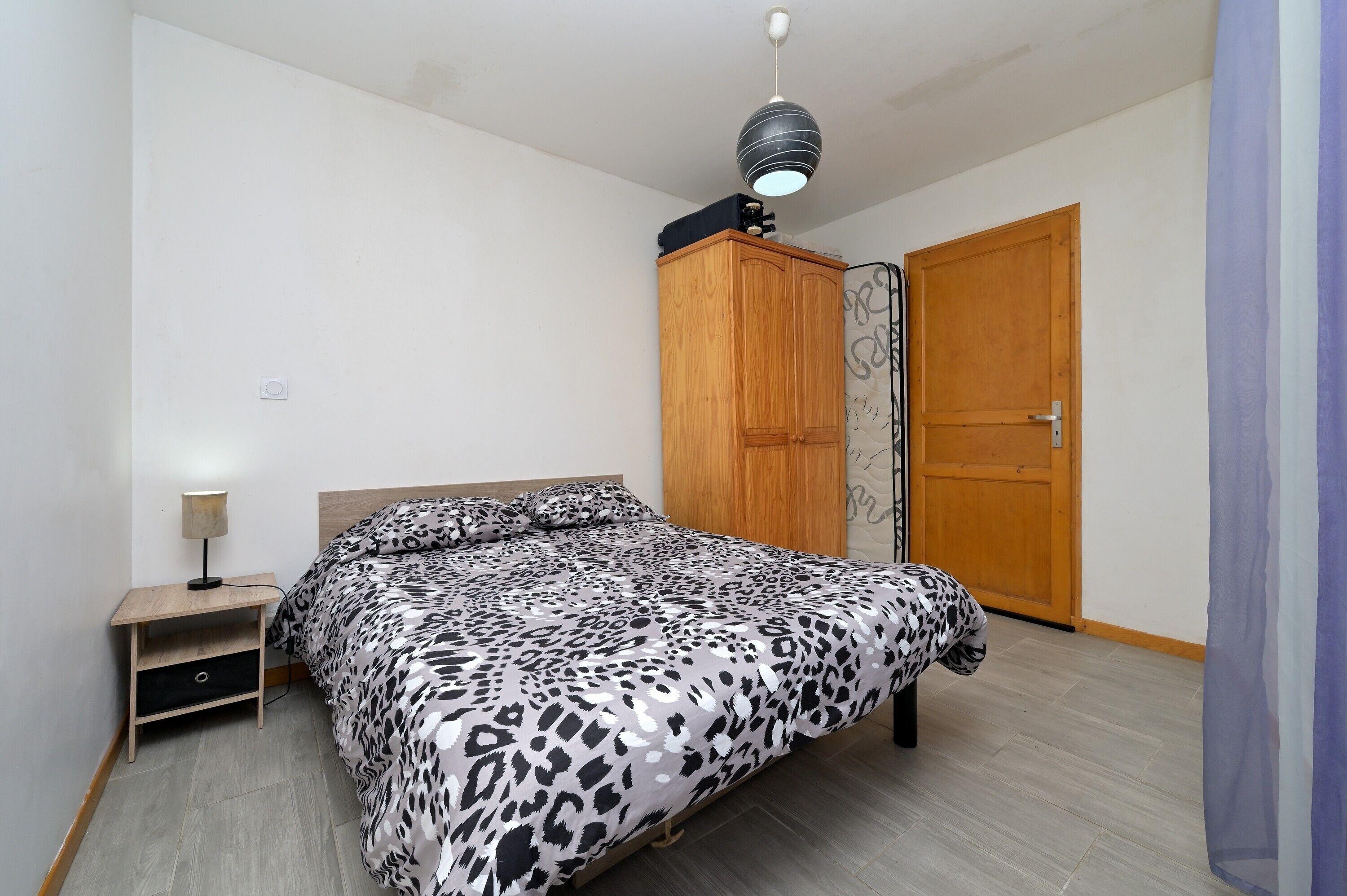 A bedroom with a bed, a wardrobe, a nightstand, and a ceiling light fixture.