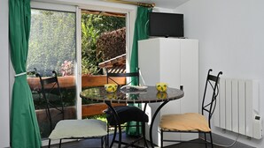 Una habitación con una mesa de vidrio, dos sillas, un televisor en la pared y vistas al exterior.