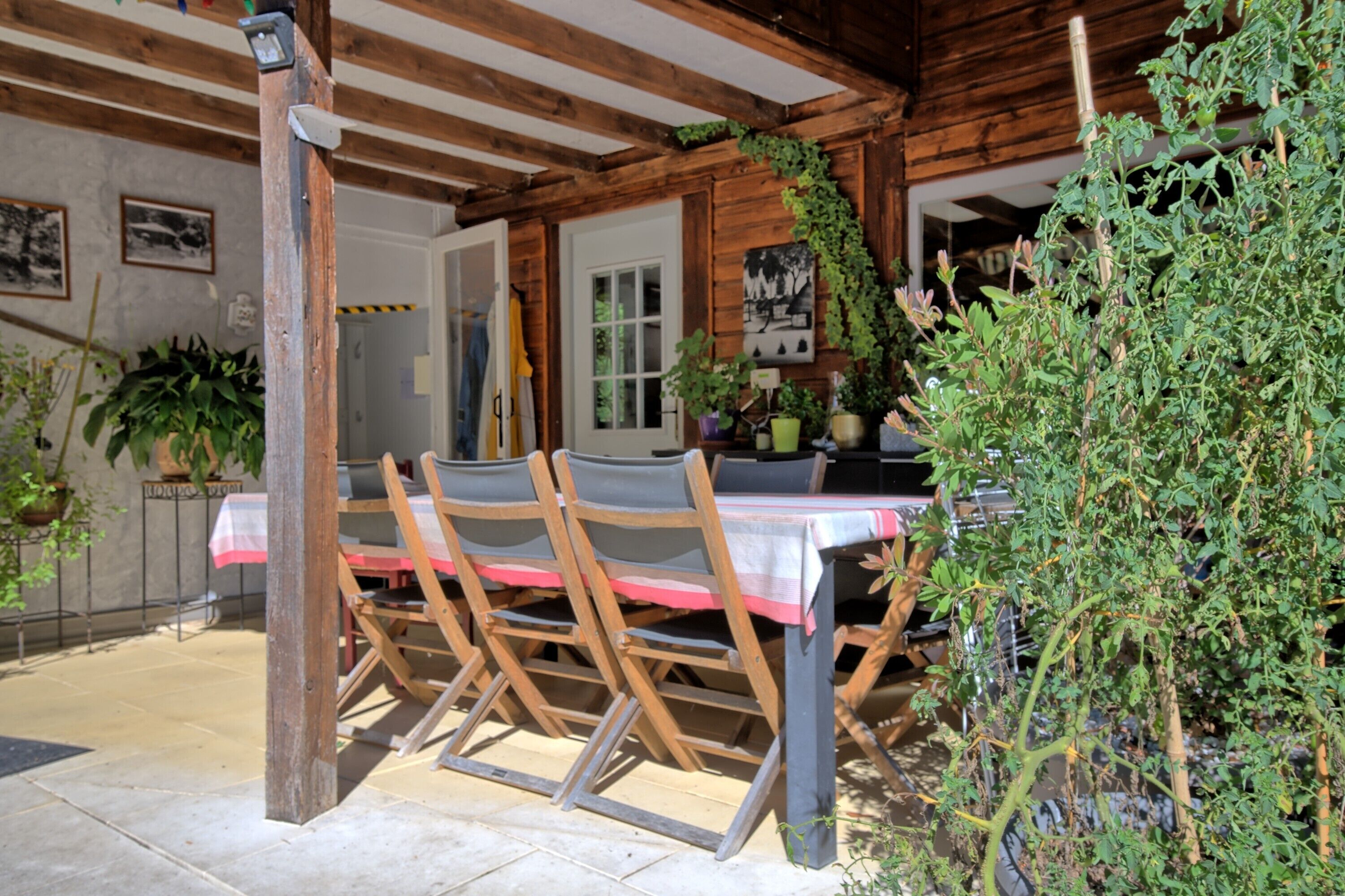 A rustic wooden dining area with a table and chairs, surrounded by potted plants and a wooden structure.