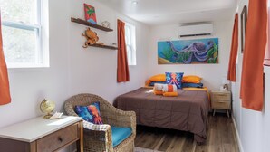 Un dormitorio con una cama, una silla de mimbre, una mesita de noche, un globo terráqueo y un cuadro en la pared.