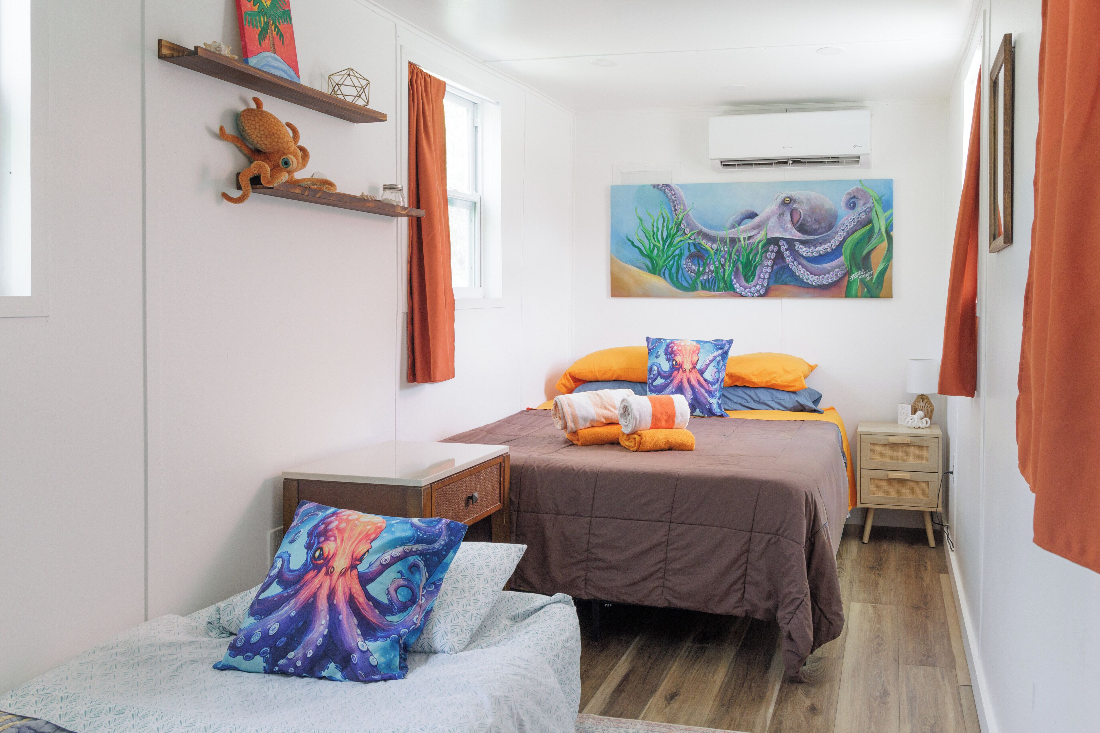 Une chambre à coucher avec deux lits, une table de chevet, une étagère murale ornée d’un objet décoratif et un tableau représentant une pieuvre.