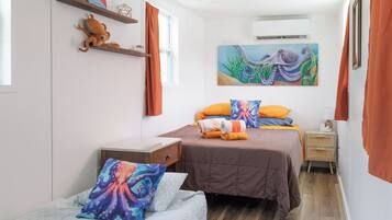 Une chambre à coucher avec deux lits, une table de chevet, une étagère murale ornée d’un objet décoratif et un tableau représentant une pieuvre.