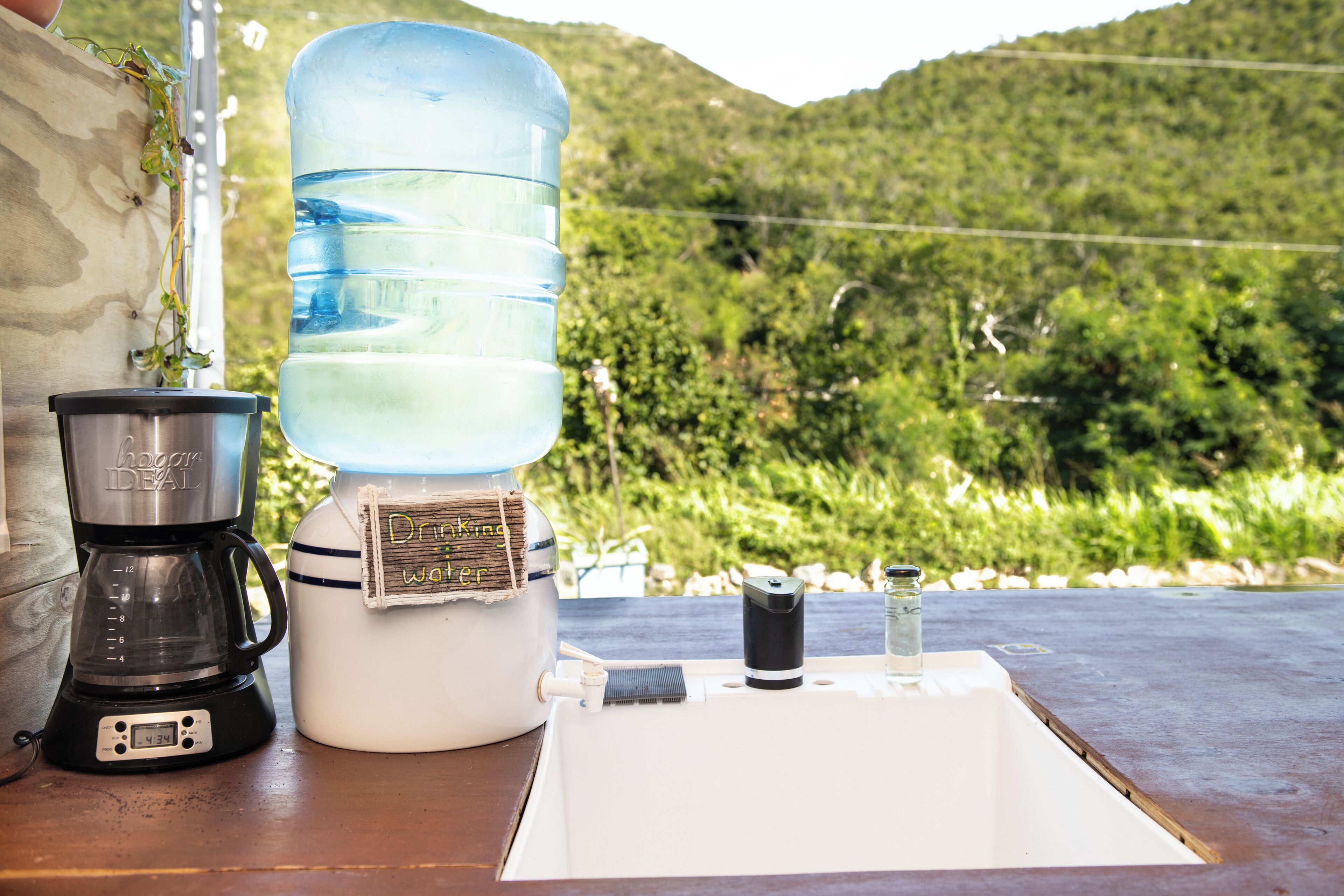 Un distributeur d’eau, une machine à café et un petit récipient sont posés sur une table, offrant une vue sur un paysage verdoyant.